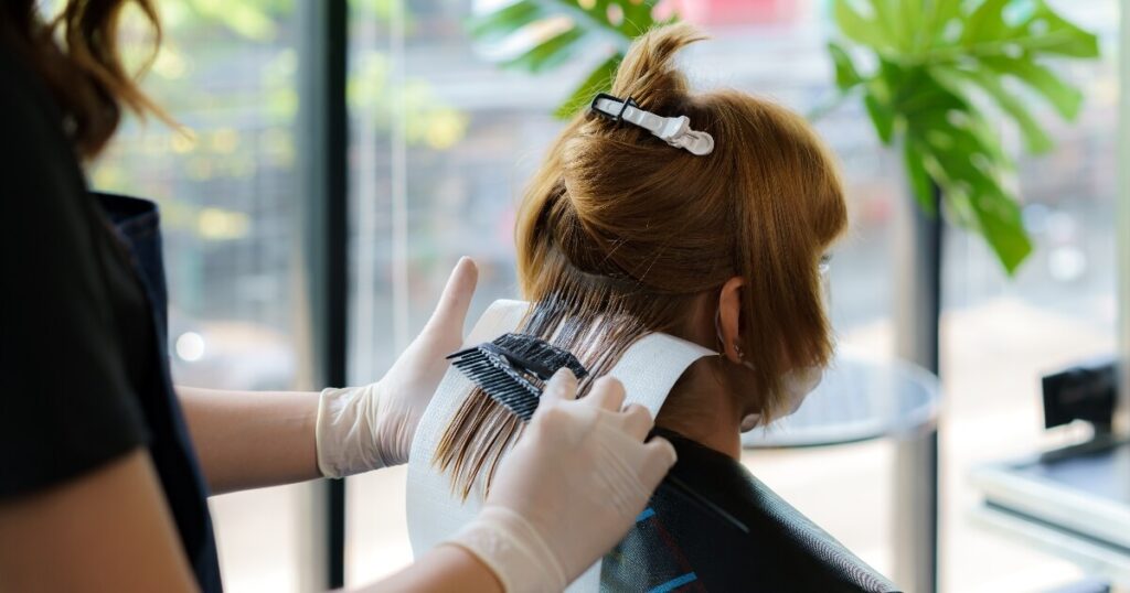 stylist-dyeing-hair-at-salon-1200-630 applying dye to dark hair in salon during daytime