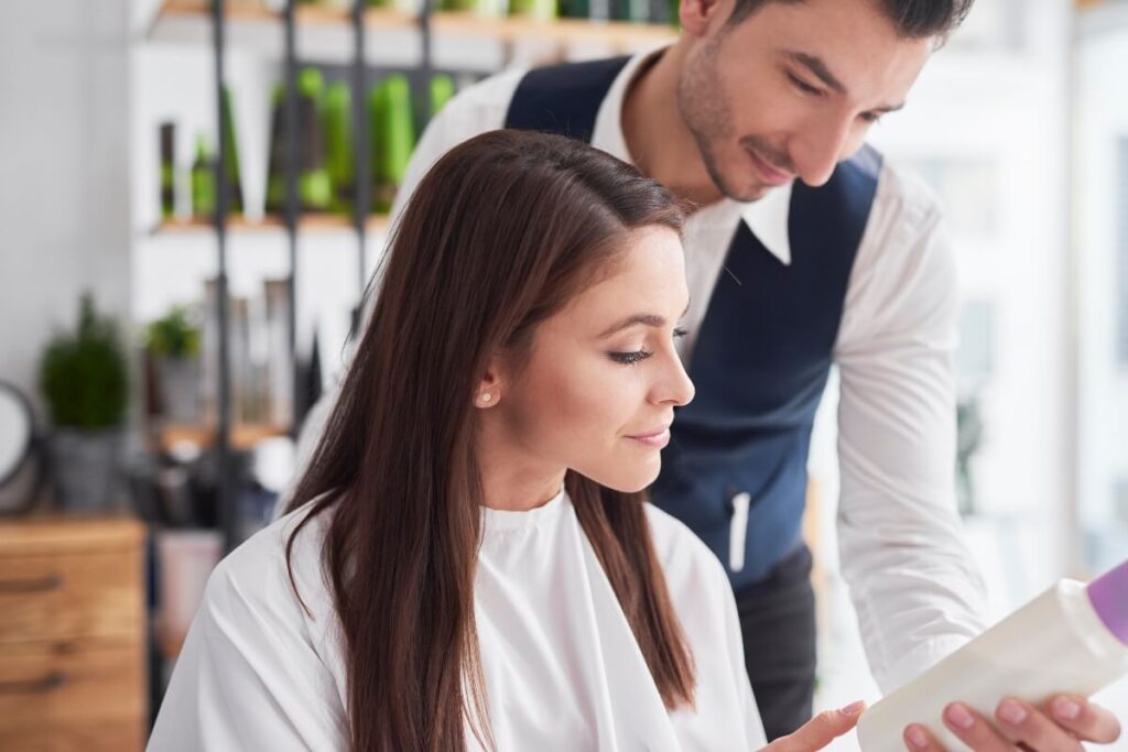 client-showing-hair-stylist-images-on-smartphone-1200-800 stylist reviewing bottle of hair product with client at salon