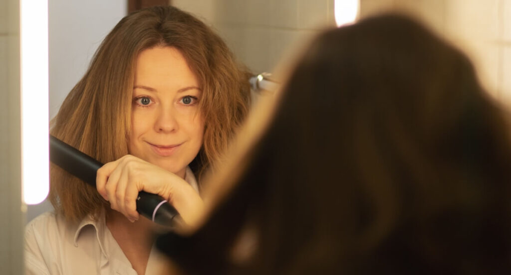 woman-with-half-of-her-hair-straightened-using-flat-iron woman smiling as she straightens her wavy hair