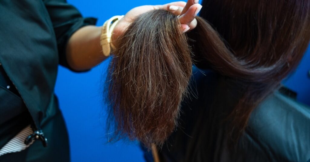 hair stylist holding long dark damaged hair