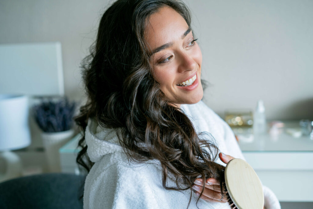 smiling brunette combing hair while wearing a bathrobe